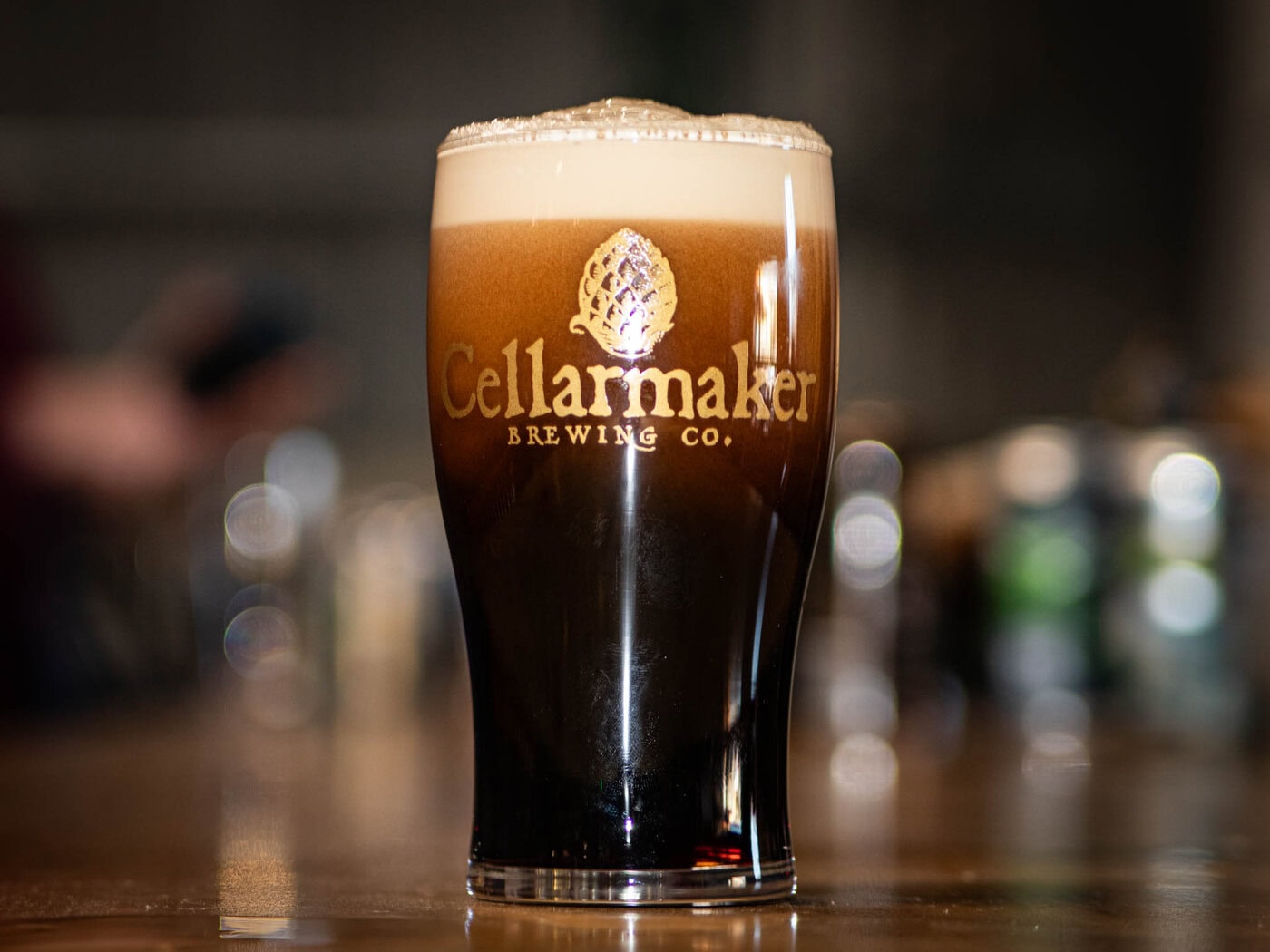 A Mt. Nelson Glass Filled With Dark Beer And A Thick, Creamy Foam Head, Labeled &Amp;Quot;Cellarmaker Brewing Co.&Amp;Quot; And Set On A Blurred Wooden Surface With A Softly Blurred Background.
