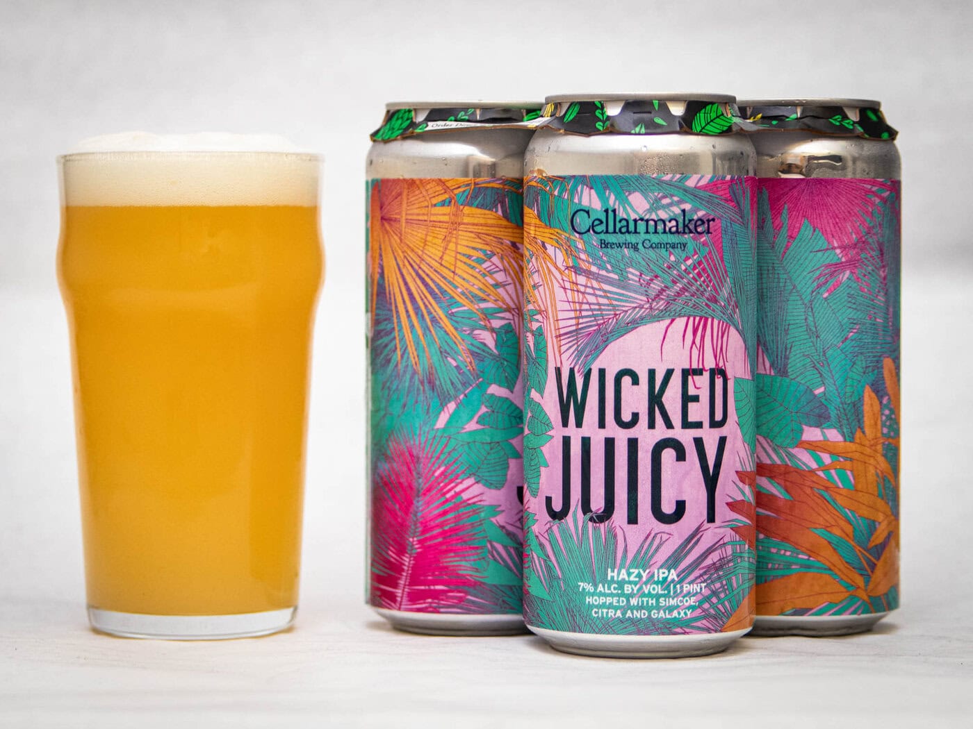 A Hazy, Golden Pint Of Wild Gooseberry Chase - Hazy Ipa Sits Beside Three Colorful Cans From Cellarmaker Brewing Company, Featuring Vibrant Tropical Leaf Designs In Pink, Orange, And Teal.