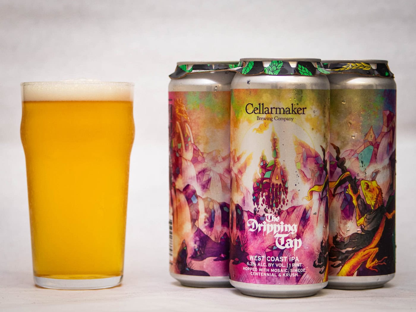 A Pint Glass Of Hazy Yellow Beer Sits Beside Four Colorful Cans Labeled &Amp;Quot;Cellarmaker Brewing Company - Wild Gooseberry Chase, Hazy Ipa,&Amp;Quot; Each Featuring Vibrant, Abstract Artwork With Purple And Gold Tones.