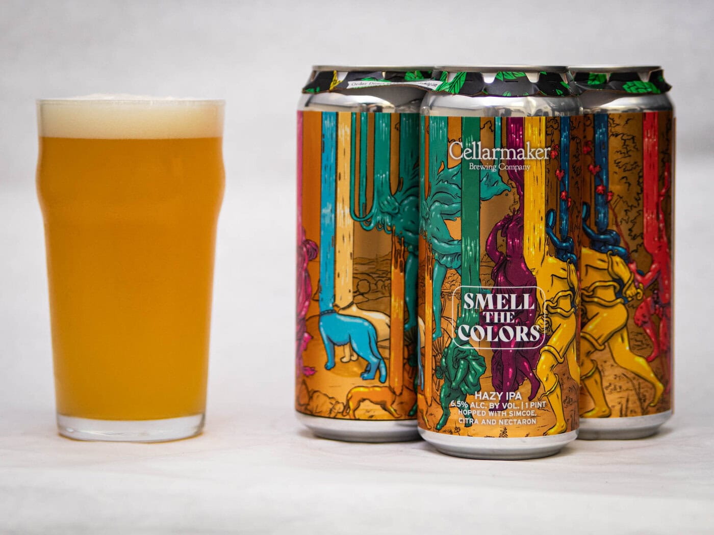 A Glass Of Pale Beer Sits Beside Three Colorful Cans Labeled “Slow Train - Wc Pale Ale” By Cellarmaker, Featuring Vibrant Abstract Artwork With Animals And Dripping Paint On The Cans.