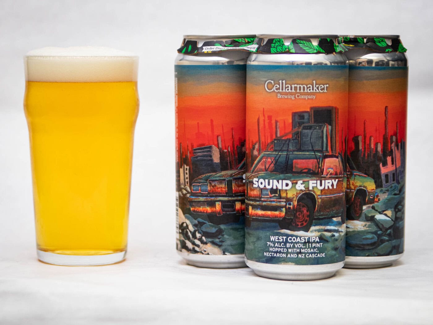 A Pint Glass Of Hazy Yellow Beer Sits Next To Three Cans Of Cellarmaker Brewing Company'S &Amp;Quot;Slow Train&Amp;Quot; West Coast Pale Ale, Showcasing Colorful Artwork Of A Ruined City And An Old Car.