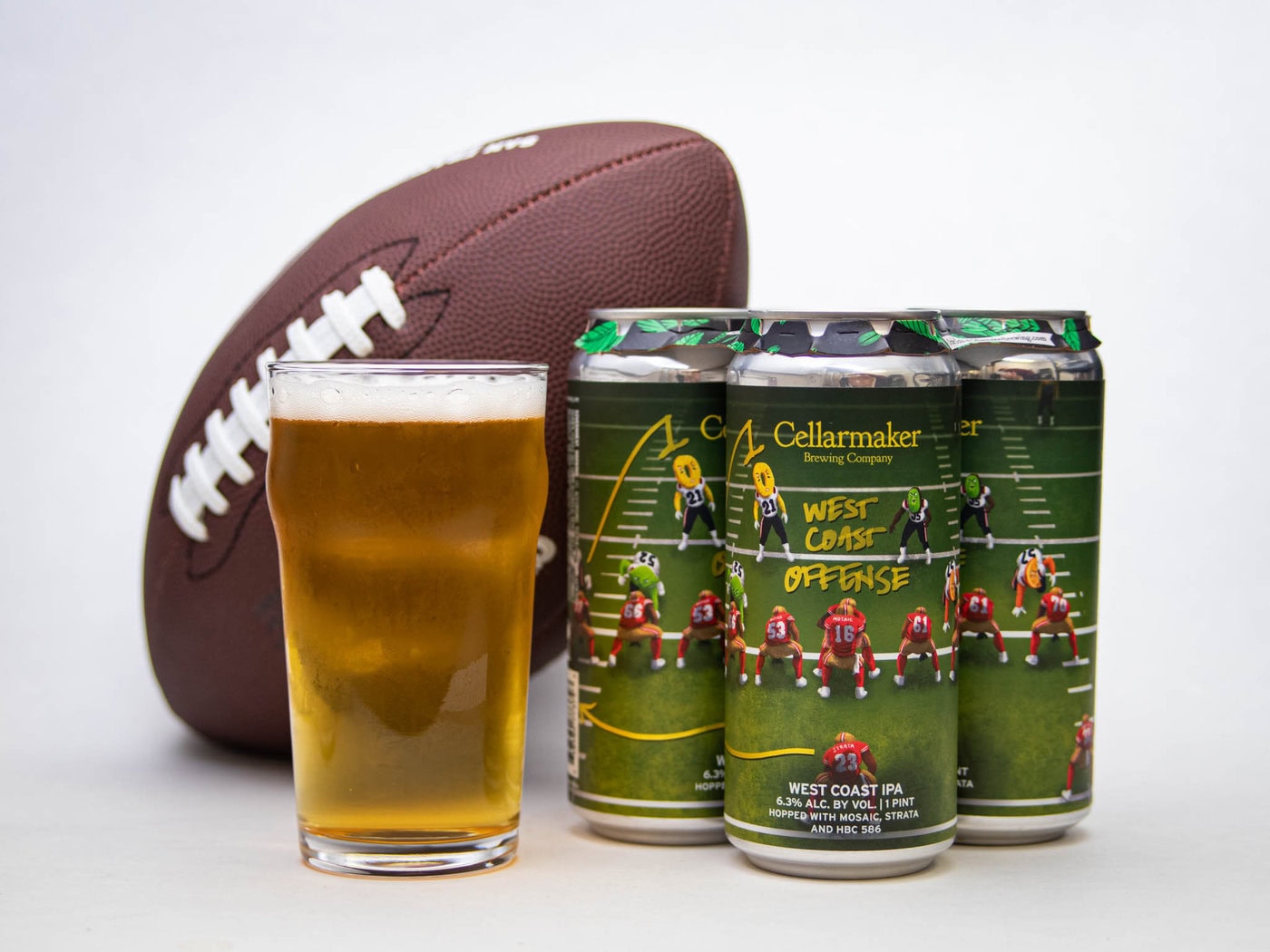 A Pint Of Beer Sits Next To Three Cans Labeled &Amp;Quot;Cellarmaker Brewing Company West Coast Offense,&Amp;Quot; Featuring A Football Field Design, With An American Football In The Background.