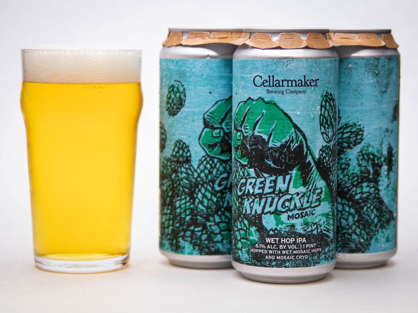 A Pint Glass Of Hazy Yellow Beer Sits Beside Three Cans Of Cellarmaker Brewing Company’s Green Knuckle Mosaic Wet Hop Ipa, Which Have Teal Labels Featuring Illustrated Green Fists And Hop Cones.
