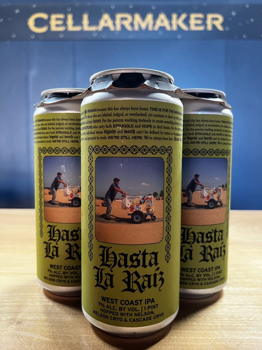 Three Cans Of &Amp;Quot;Hasta La Raiz&Amp;Quot; West Coast Ipa Sit On A Wooden Surface. The Cans Feature A Yellow Label With An Image Of A Man Pushing A Decorated Cart And The Words &Amp;Quot;Cellarmaker&Amp;Quot; On A Blue Background Behind Them.