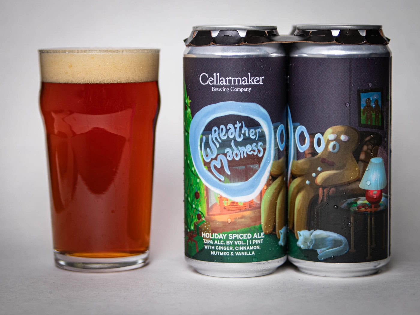 A Pint Glass Of Amber Beer Sits Beside Two Cans Labeled “Cellarmaker Brewing Company Weather Madness Holiday Spiced Ale,” Featuring A Whimsical Gingerbread Figure On A Couch With Festive Colors.