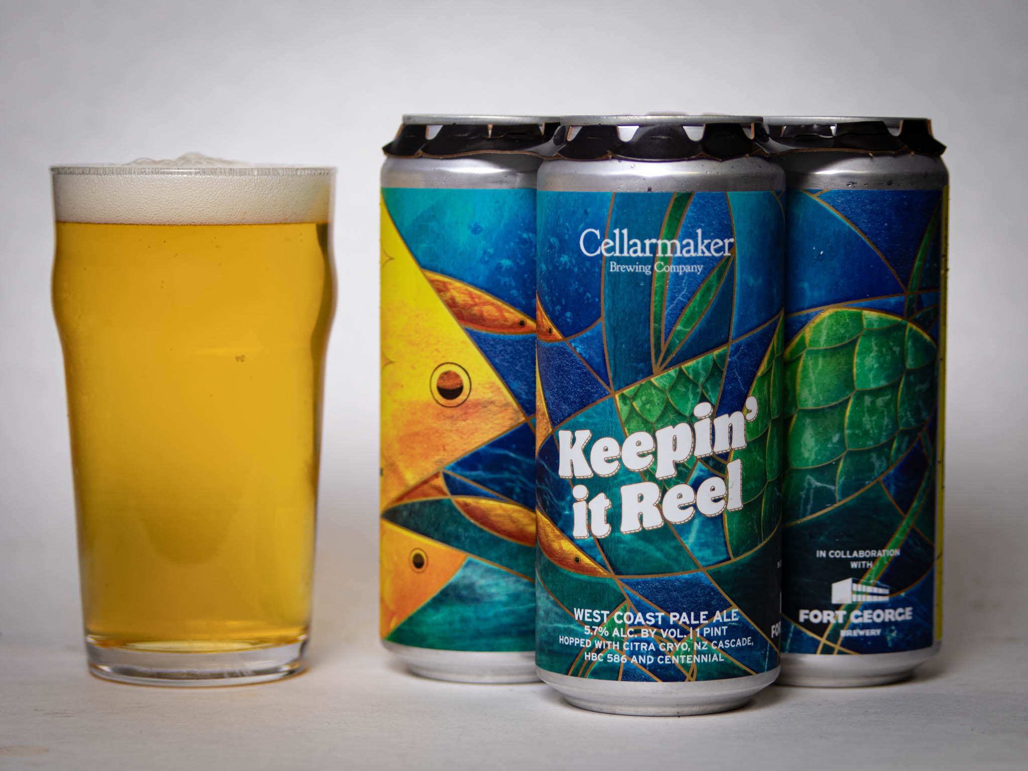 A Pint Glass Of Pale Beer Sits Next To Three Colorful Cans Of Cellarmaker Brewing Company'S &Amp;Quot;Keepin' It Reel&Amp;Quot; West Coast Pale Ale, Featuring Abstract Fish Scale Artwork On The Labels.